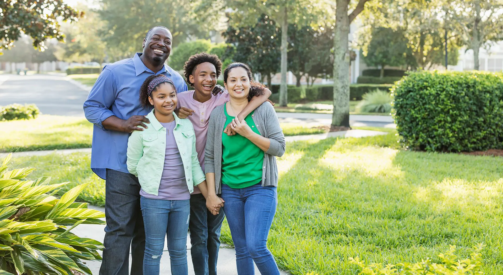 A smiling family of four enjoys a sunny green park, with one child proudly displaying their new braces-free smile from Wink Orthodontics in Prosper, TX.