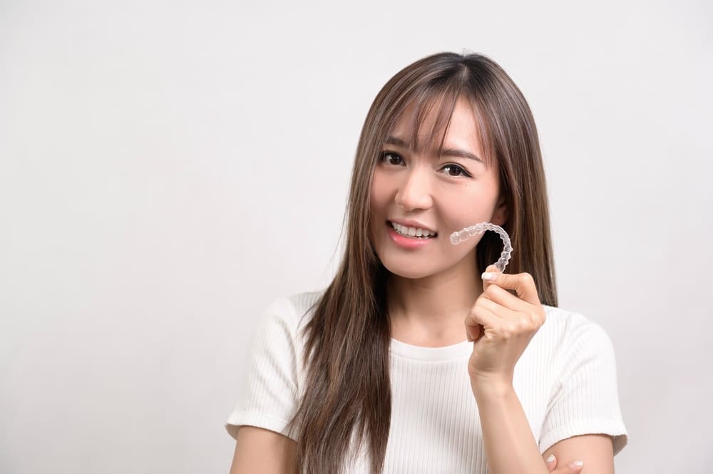 young smiling woman holding invisalign clear aligners - Can Invisalign Fix Overbite in Prosper and Colleyville, TX.