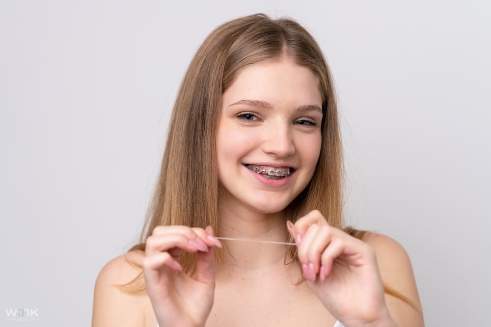 teenager russian girl with metal braces and floss isolated white background - How to Floss with Braces in Prosper and Colleyville, TX