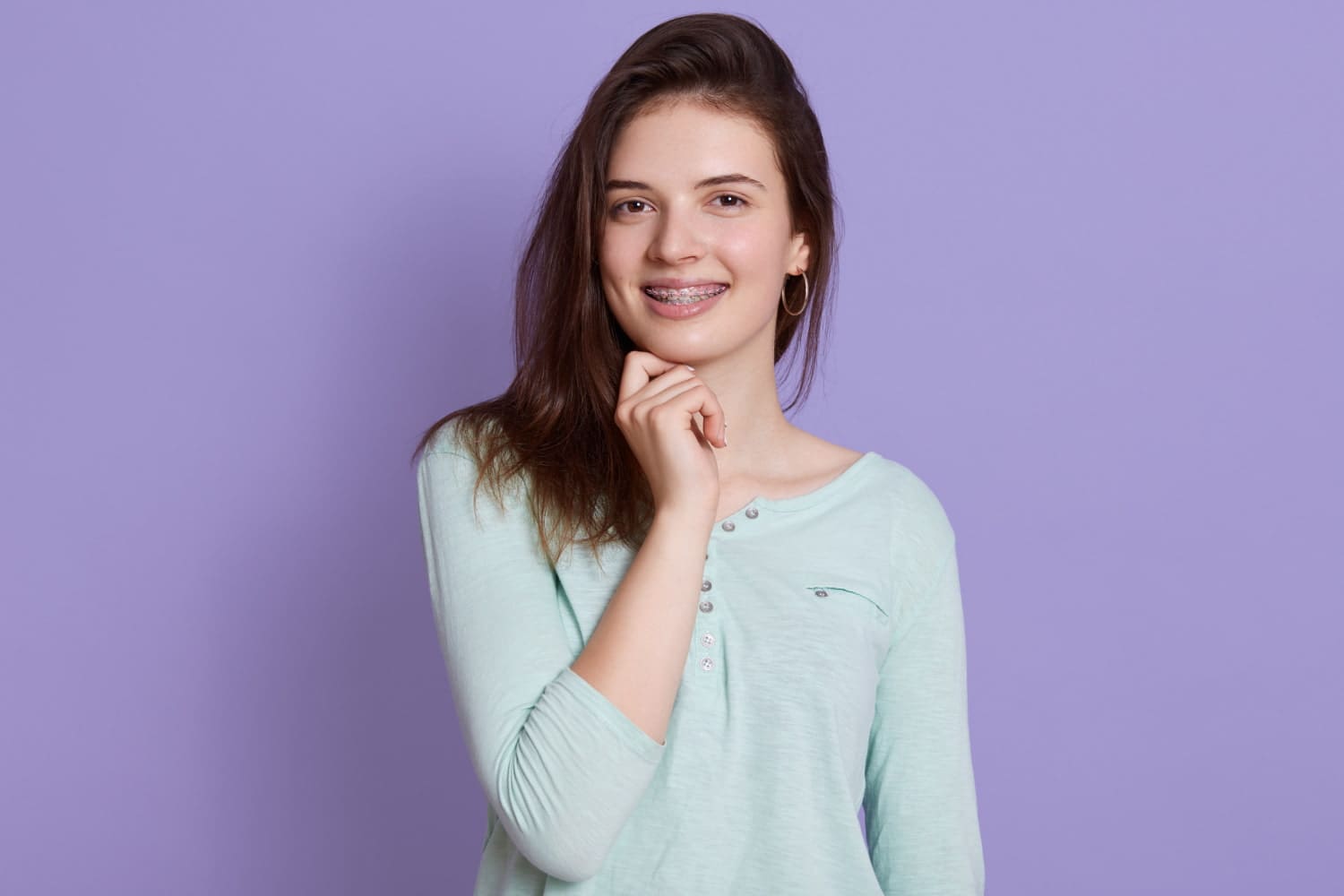 Wink Orthodontics Smiling young person with braces poses in a green shirt, thinking about Braces Cost at Wink Orthodontics in Prosper or Colleyville, TX.