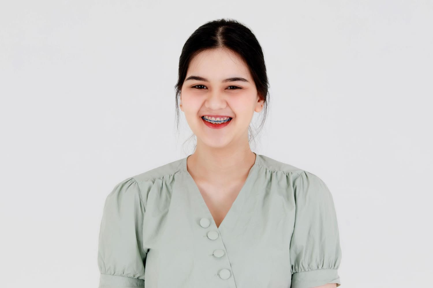 Wink Orthodontics A young woman with dark hair in a light green blouse smiles after learning about Braces Cost at Wink Orthodontics in Prosper or Colleyville, TX.