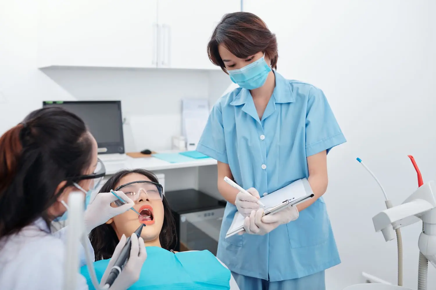 Dr. Mohammed Al-Zainal and Dr. Mo Idilbi: Orthodontist in Colleyville TX At Wink Orthodontics in Colleyville, TX, a dentist examines a patient’s teeth as an assistant takes notes nearby.