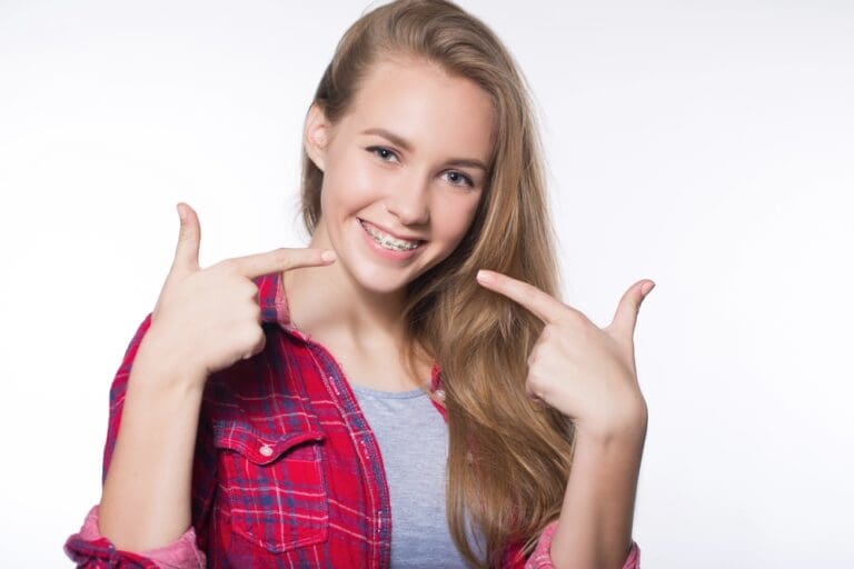 beautiful young blondie girl showing her metal braces isolated white - How to Get Braces Glue Off Teeth in Prosper and Colleyville, TX