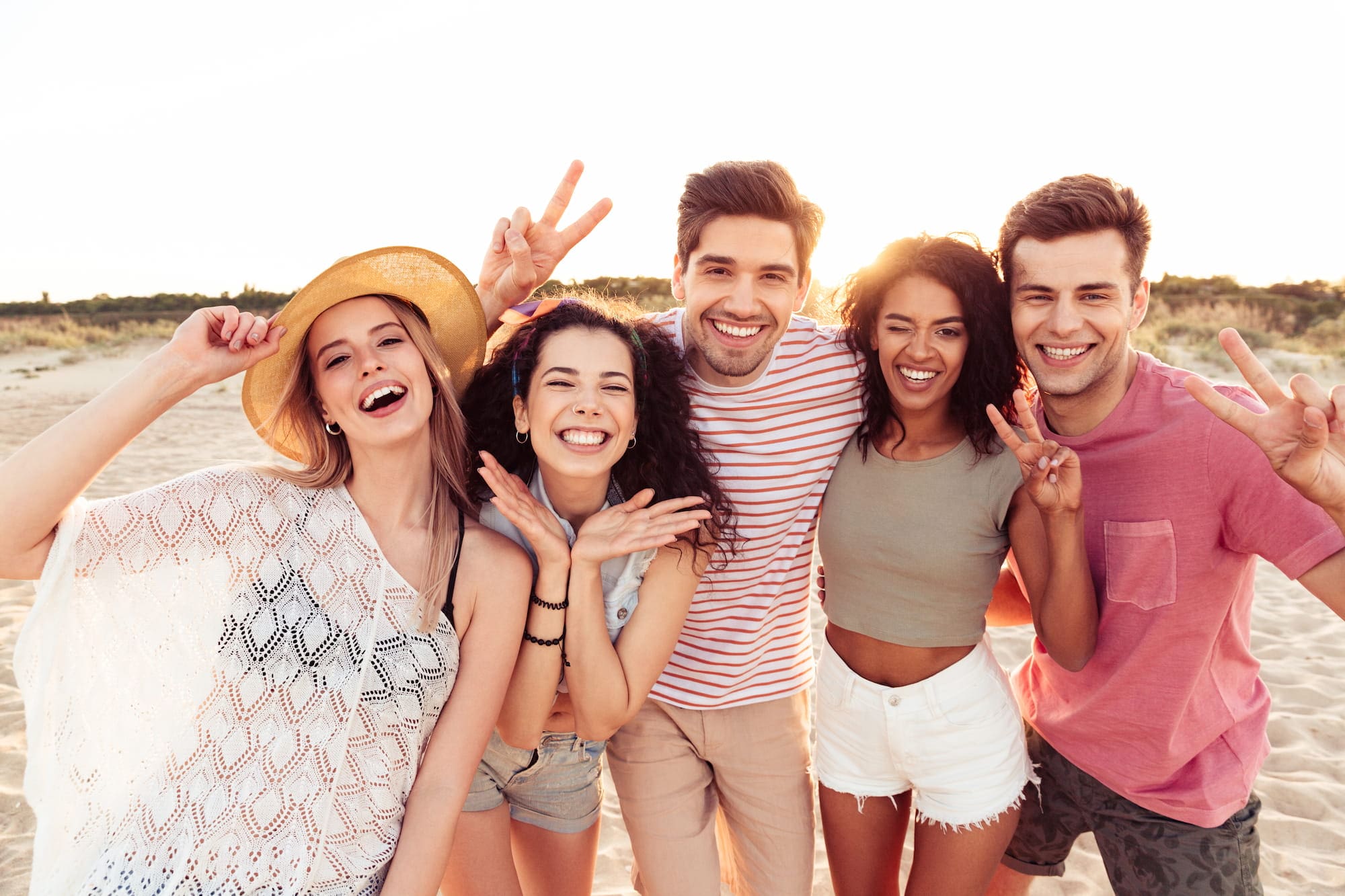 On a sunny beach with greenery, five young adults in Brava Braces from Wink Orthodontics in Prosper or Colleyville, TX pose together.